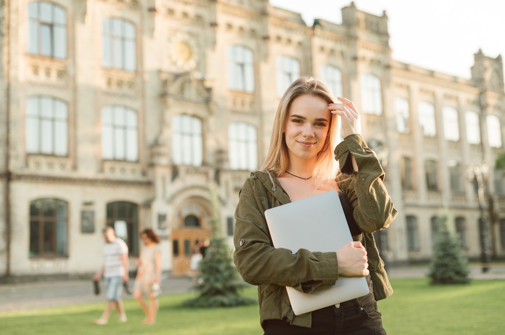 student outside accommodation holding laptop