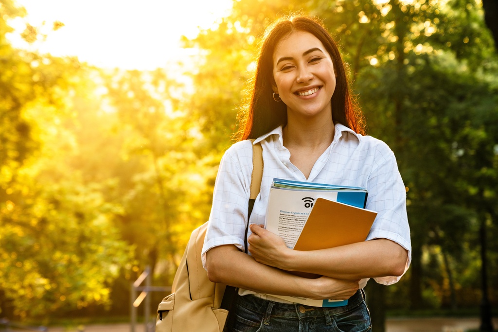 student carrying books through park
