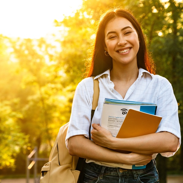 student carrying books through park