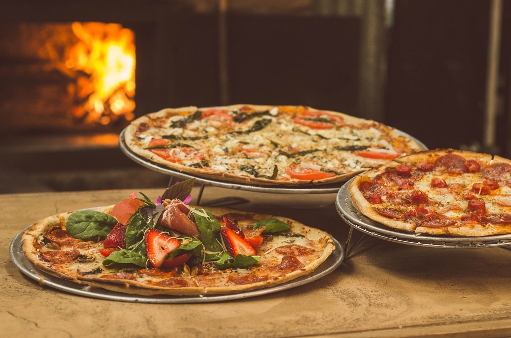 three pizzas next to stone oven